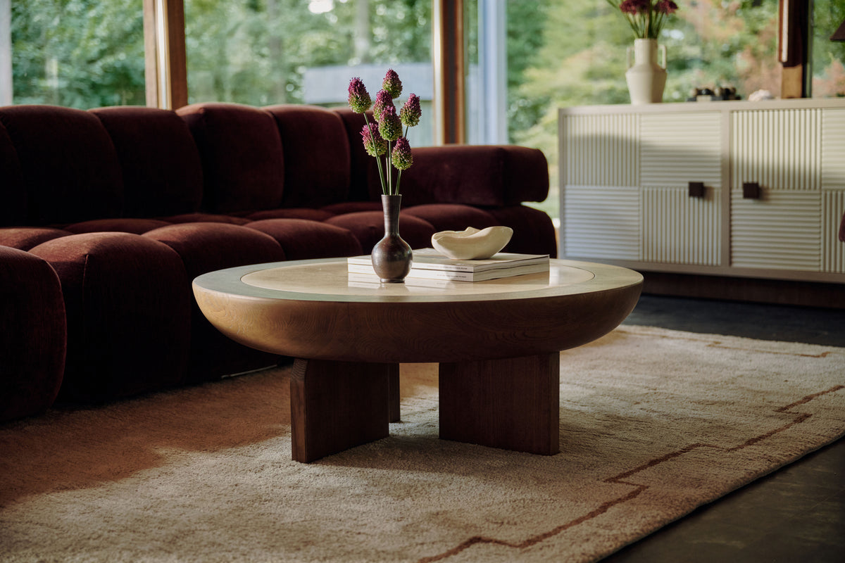 table basse Saturne ronde en bois et canapé modulable bordeaux dans un salon vitré