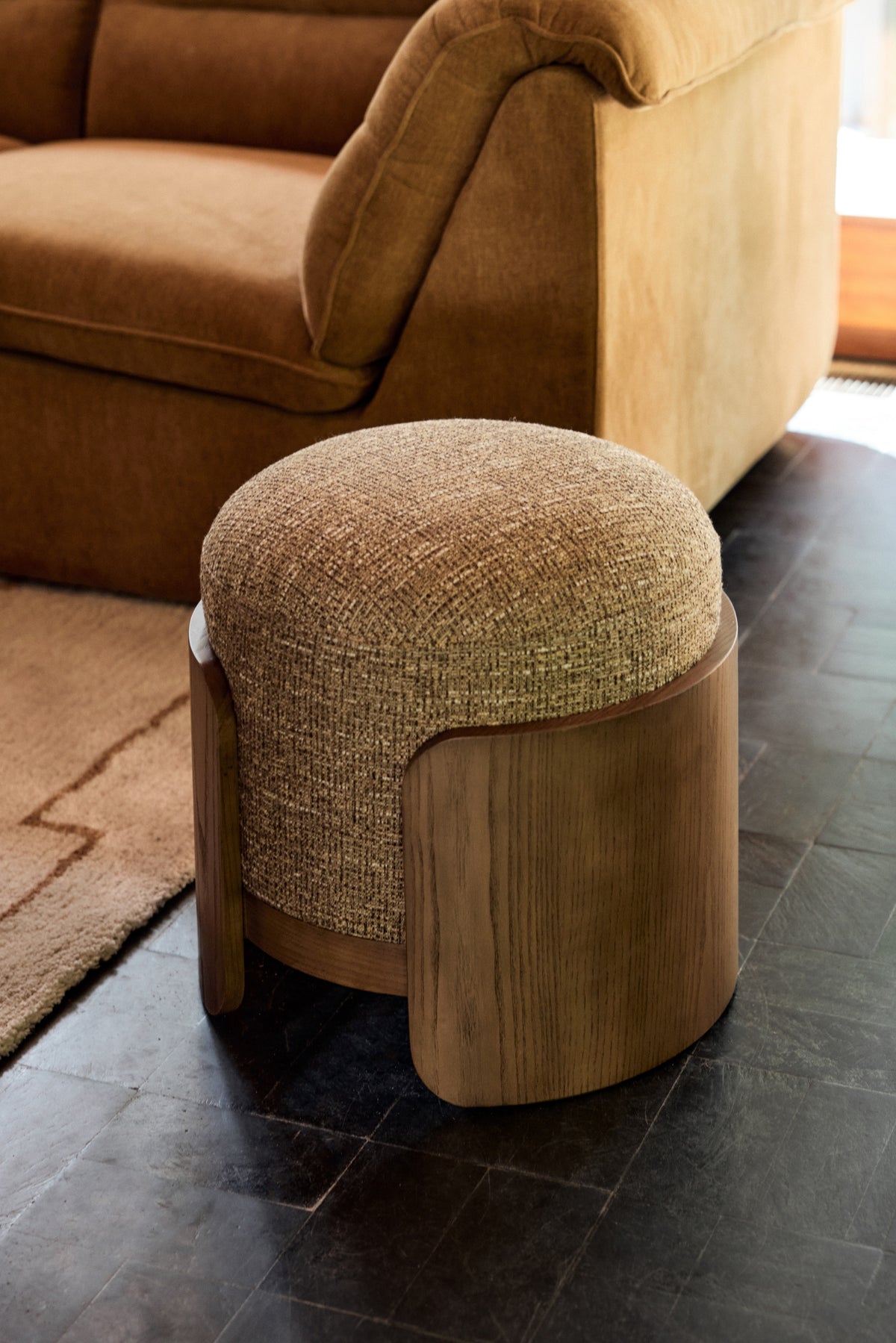 pouf Elipse en tissu chiné ocre et joues en bois cintré devant le canapé Pulp