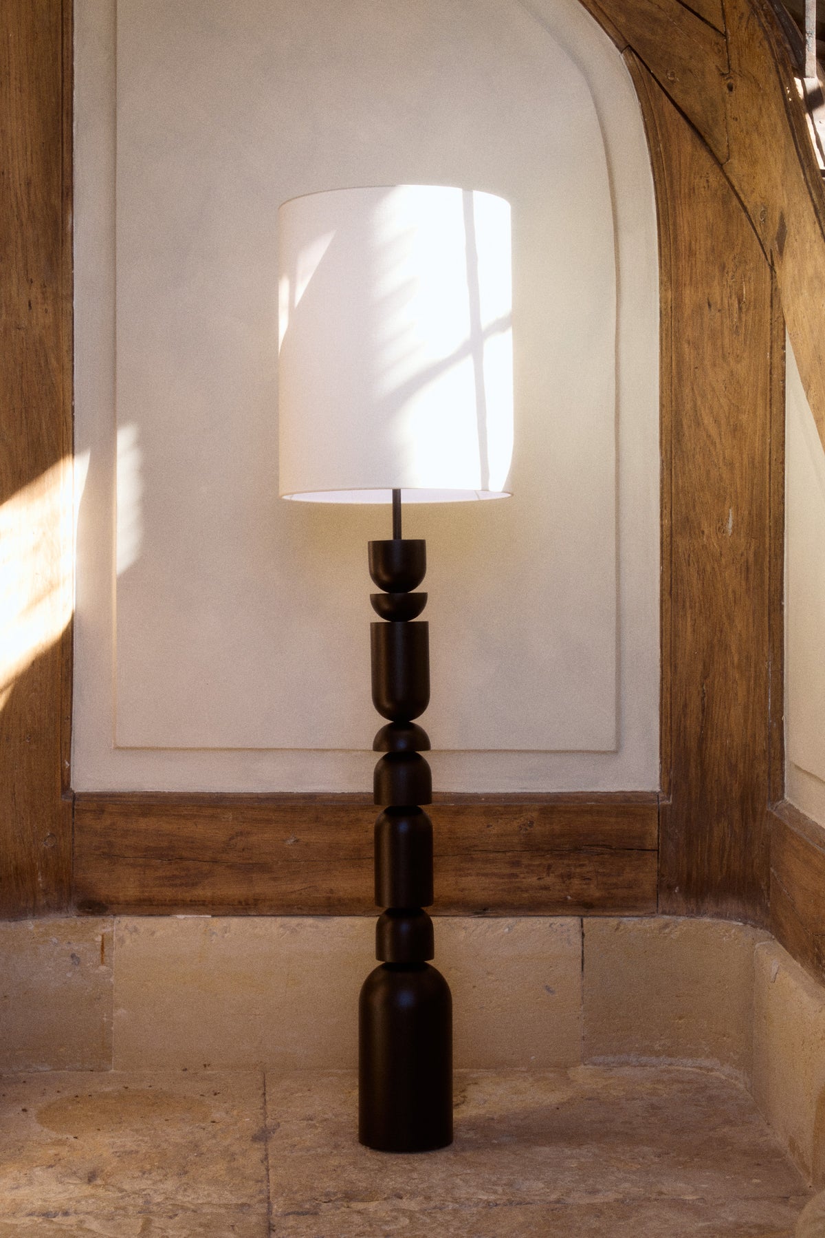 lampadaire Tinga - bois tourné noir et abat-jour lin blanc - vue de face alcôve pierre